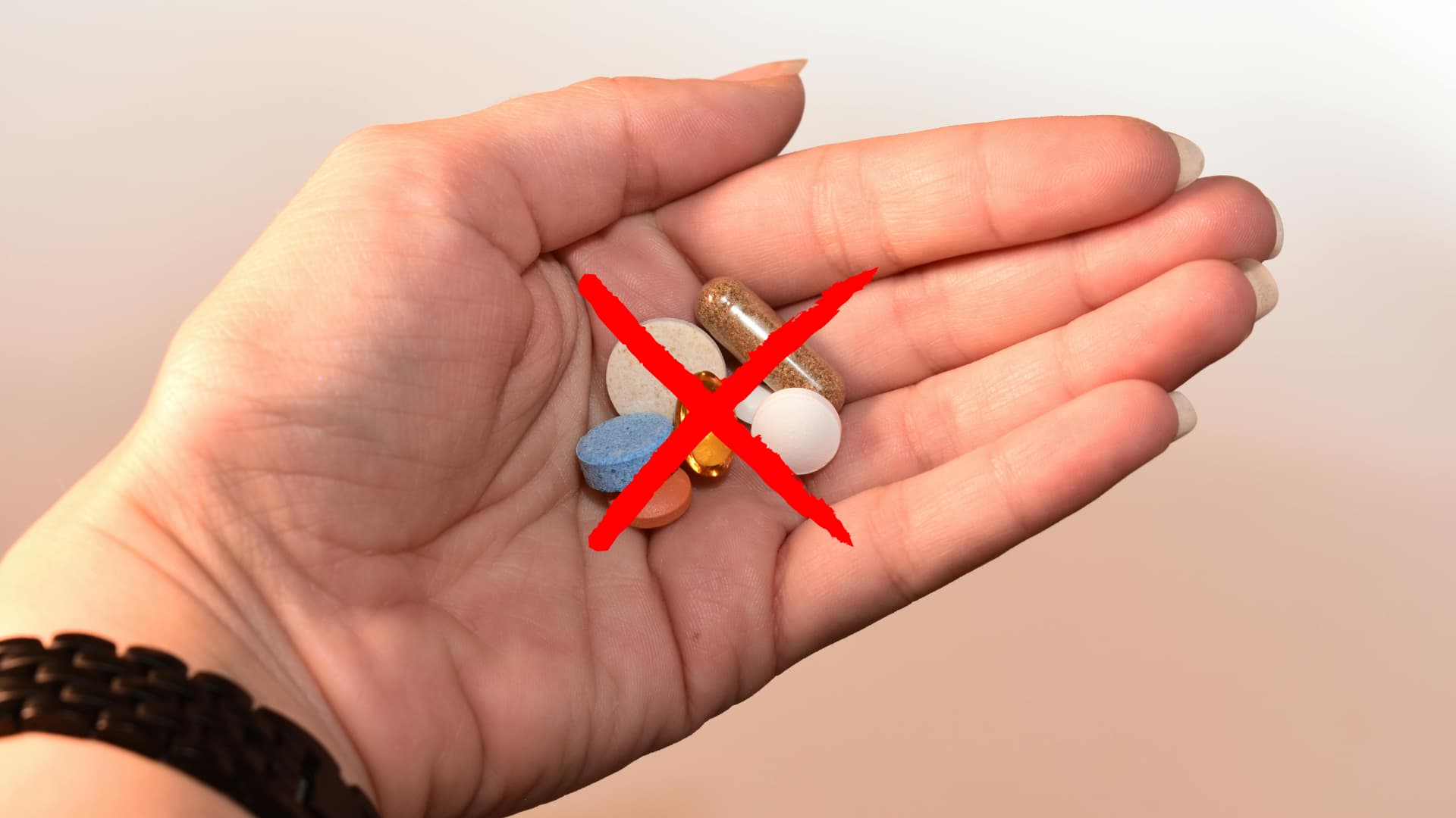 Hand holding colorful pills with a large red X symbolizing no prescriptions needed