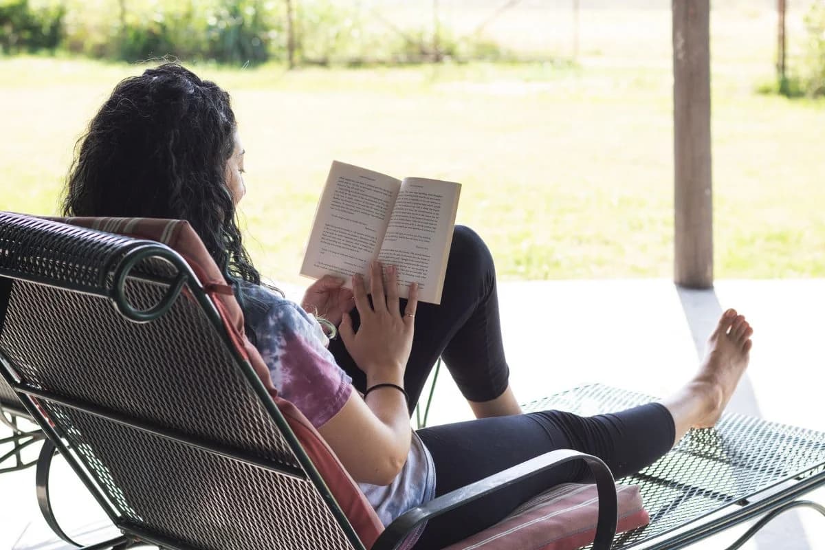 Person relaxing in a wicker chair outdoors with feet propped up, reading a book, enjoying a peaceful evening